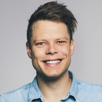 Portrait von Nico Brugger in einem hellblauen Jeans-Hemd vor einem neutralen, grauen Hintergrund